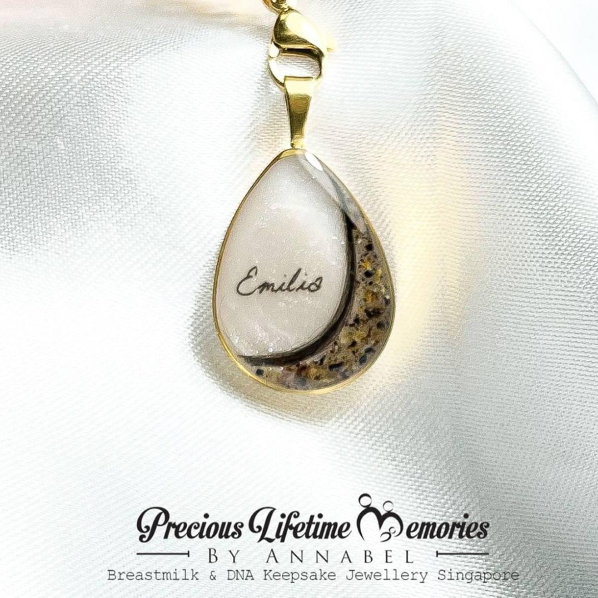 Teardrop-shaped pendant with gold chain on white fabric, branded 'Precious Lifetime Memories by Annabel'.