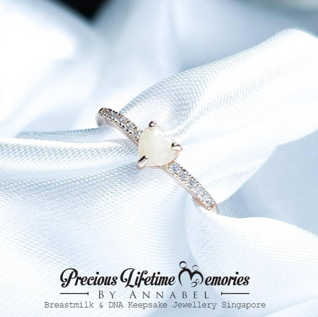 Delicate breastmilk ring with a central gemstone on a white fabric background, featuring 