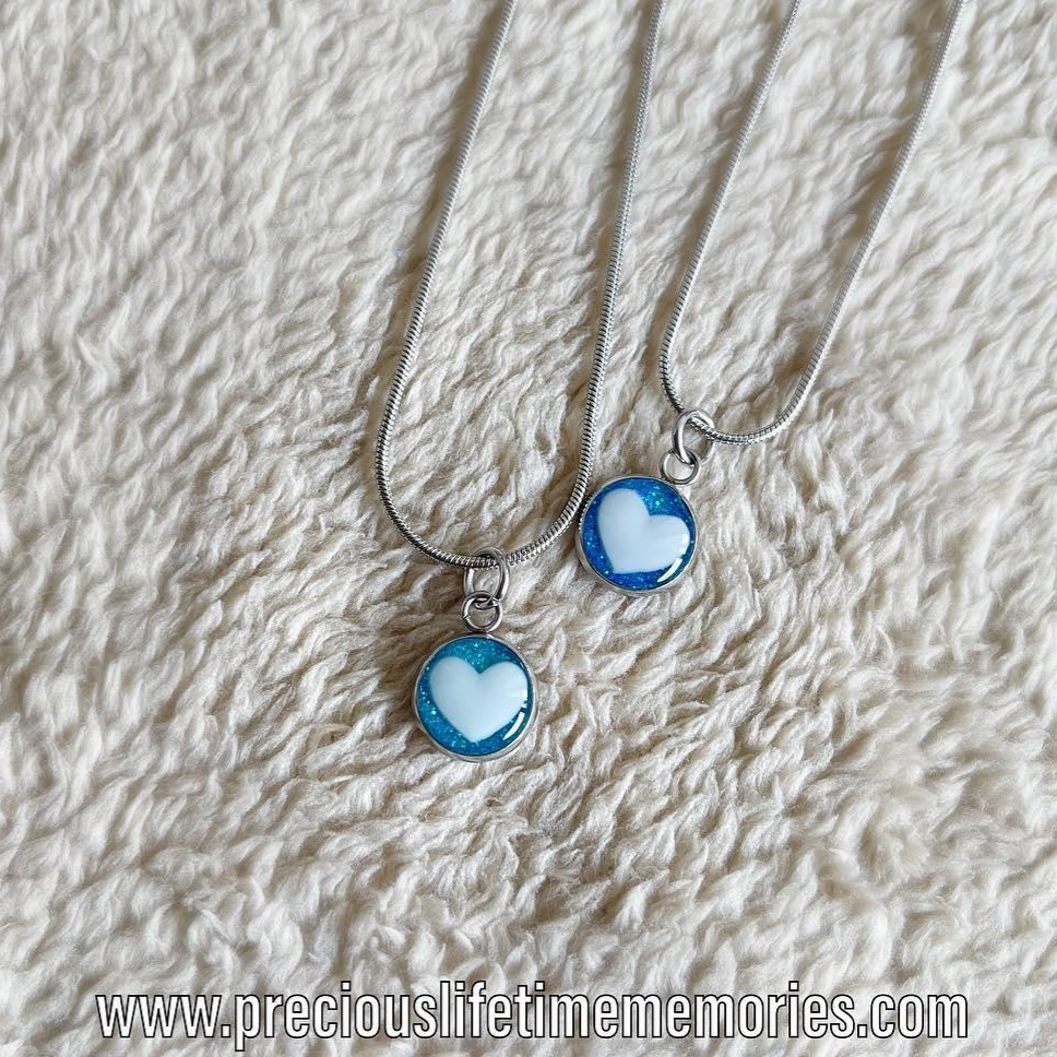Necklace with heart-shaped pendants on a textured beige surface, featuring the brand 'preciouslifetimememories'.