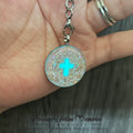 Necklace with a round pendant featuring a blue cross held in a hand.