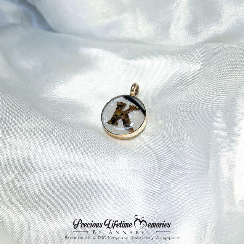 Gold pendant with a black and white design on a white satin background, featuring 'Precious Lifetime Memories by Annabel'.