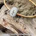 Gold bracelet with a silver clasp on a piece of driftwood, featuring a website address.