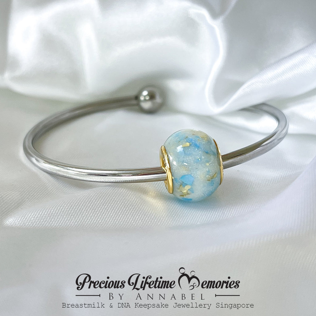 Silver bracelet with a blue and gold bead on a white satin background, featuring 'Precious Lifetime Memories by Annabel'.