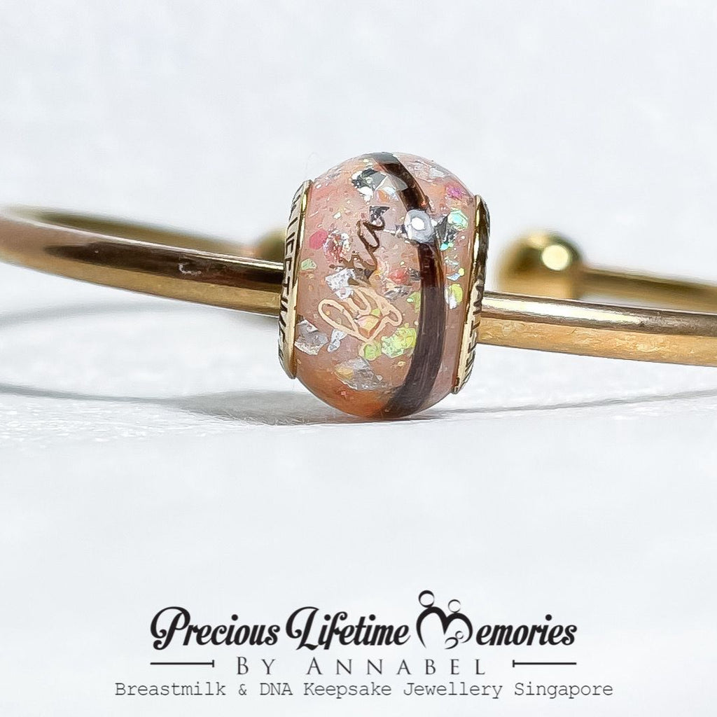Gold bangle with a decorative clasp on a white background, featuring 'Precious Lifetime Memories by Annabel'.