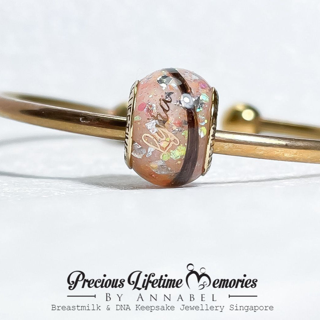 Gold bangle with a decorative clasp on a white background, featuring 'Precious Lifetime Memories by Annabel'.