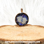 Jewelry pendant with a blue and white design on a wooden surface, featuring the website www.preciouslifetimememories.com.