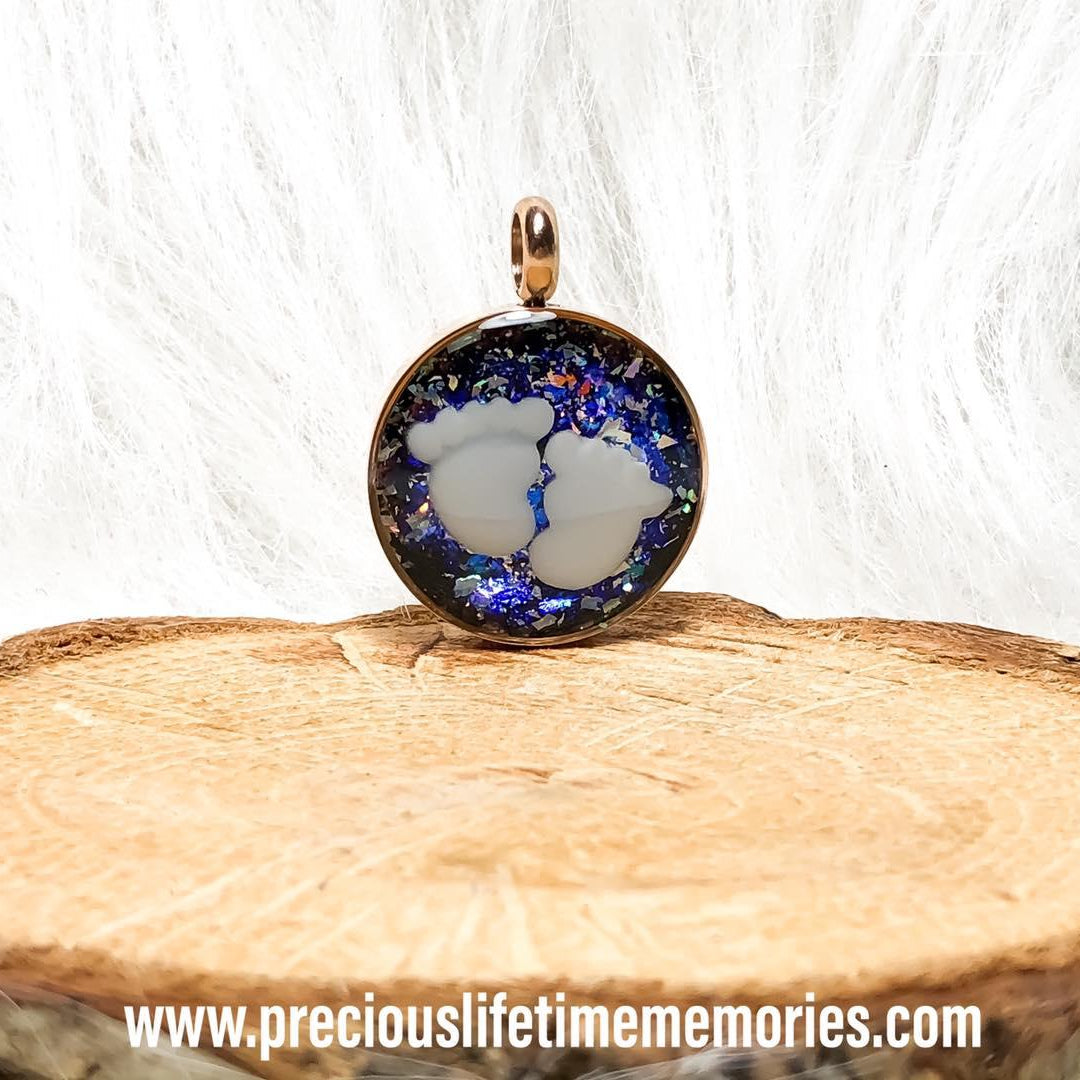 Jewelry pendant with a blue and white design on a wooden surface, featuring the website www.preciouslifetimememories.com.
