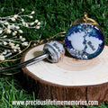 Two keychains on a wooden stump with grass in the background, breastmilk charm