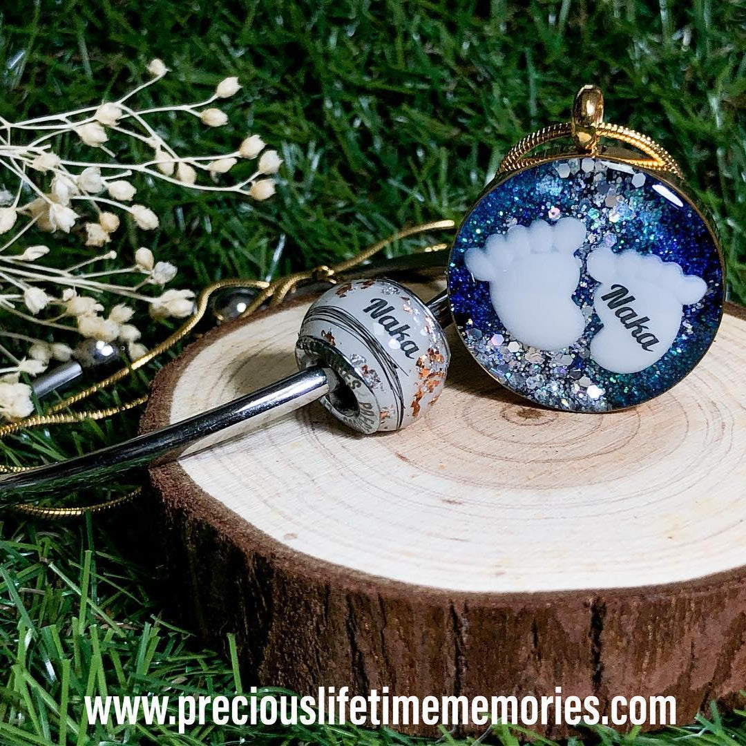 Two keychains on a wooden stump with grass in the background, breastmilk charm
