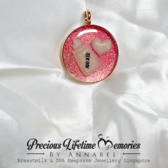 Pink glittery pendant with heart designs on a white fabric background, branded 'Precious Lifetime Memories by Annabel'.