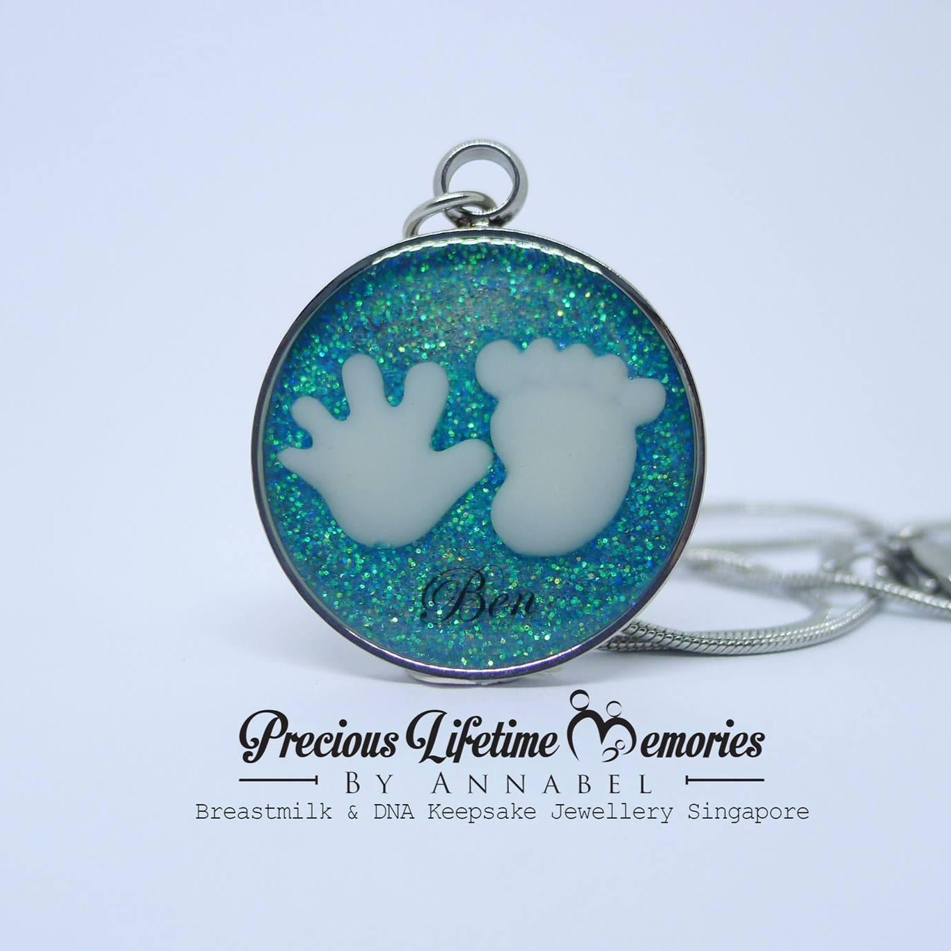 Necklace with a round pendant featuring baby hand and footprints on a blue glittery background, branded 'Precious Lifetime Memories by Annabel'.