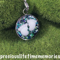 Round decorative charm with white paw prints on a green grass photo background breastfeeding jewellery