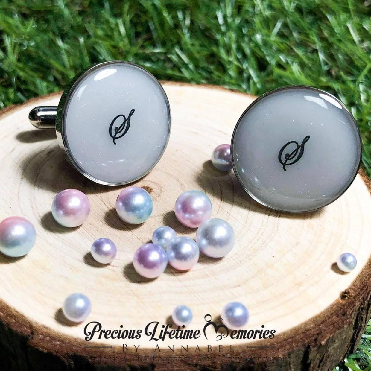 Cufflinks with a leaf design on a wooden block with pearls, set against a grassy background.
