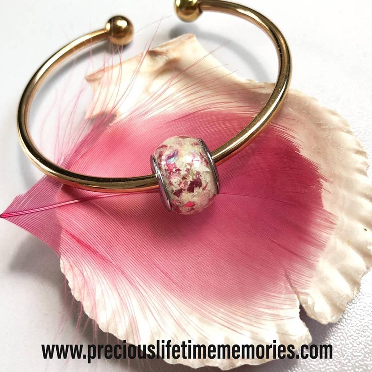 Gold bracelet with a cremation ashes pink bead on a pink shell against a white background