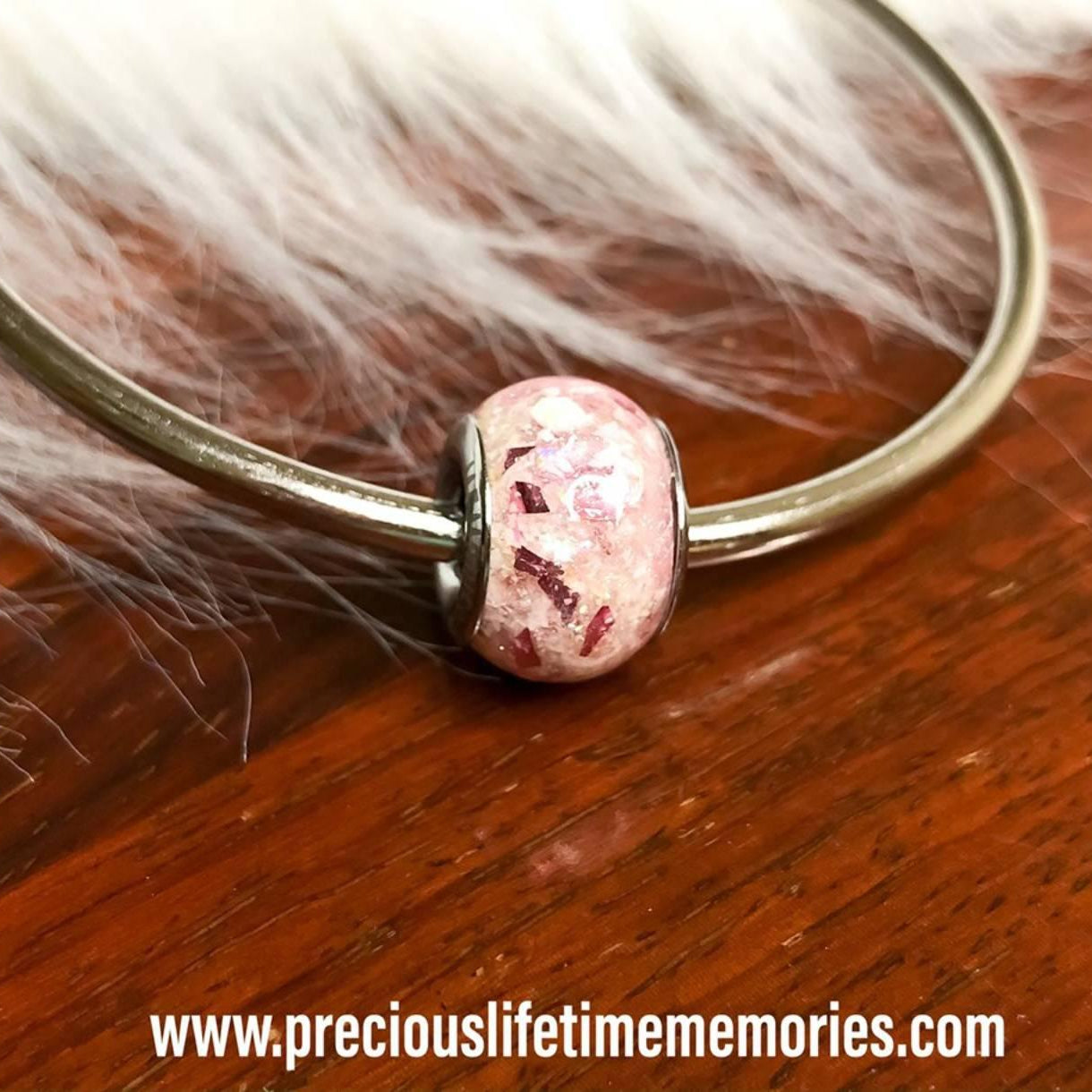 Bracelet with a pink pandora charm bead on a wooden surface with fur