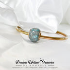 Gold bracelet with a blue gemstone on with cremation ashes, featuring 'Precious Lifetime Memories by Annabel'.