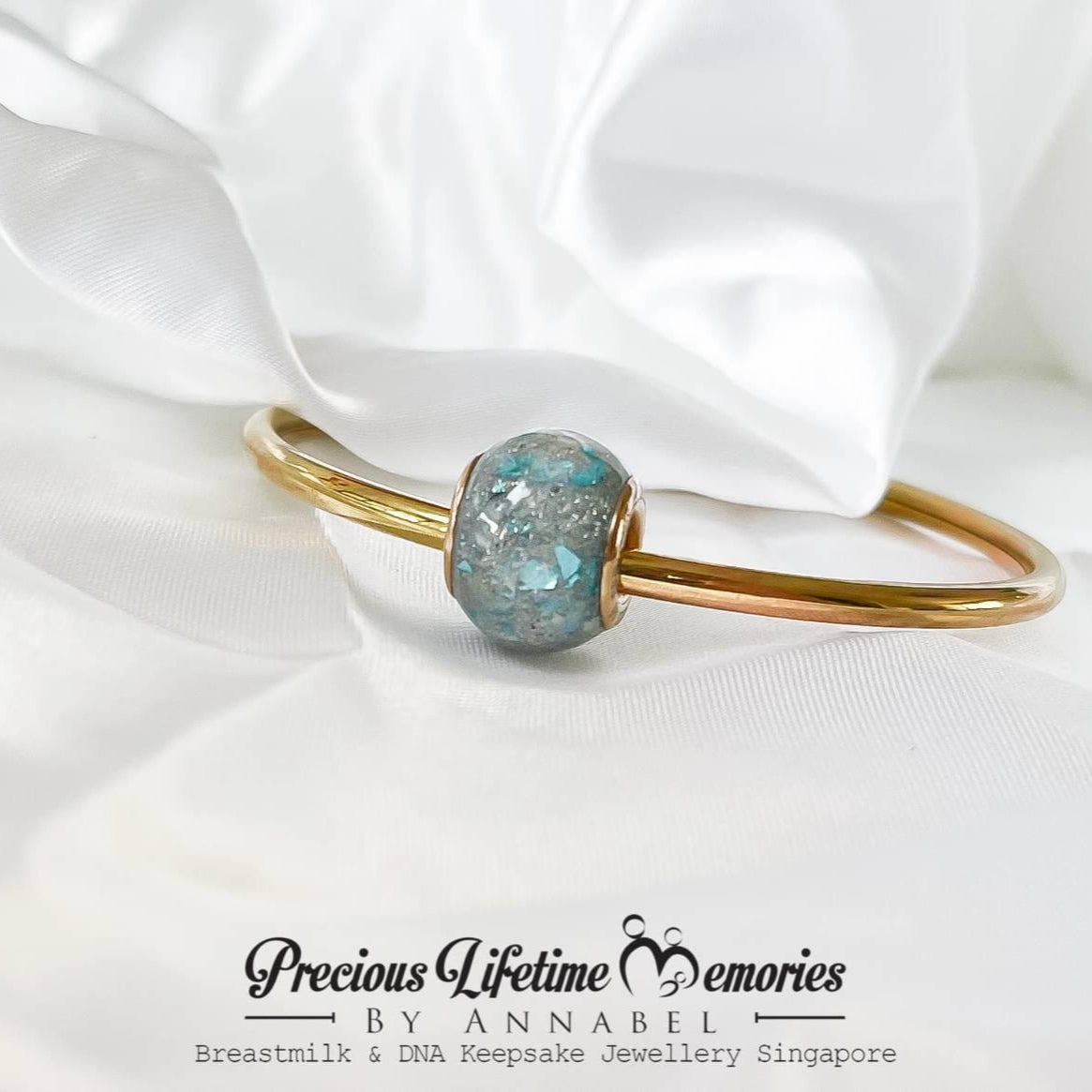 Gold bracelet with a blue gemstone on with cremation ashes, featuring 'Precious Lifetime Memories by Annabel'.