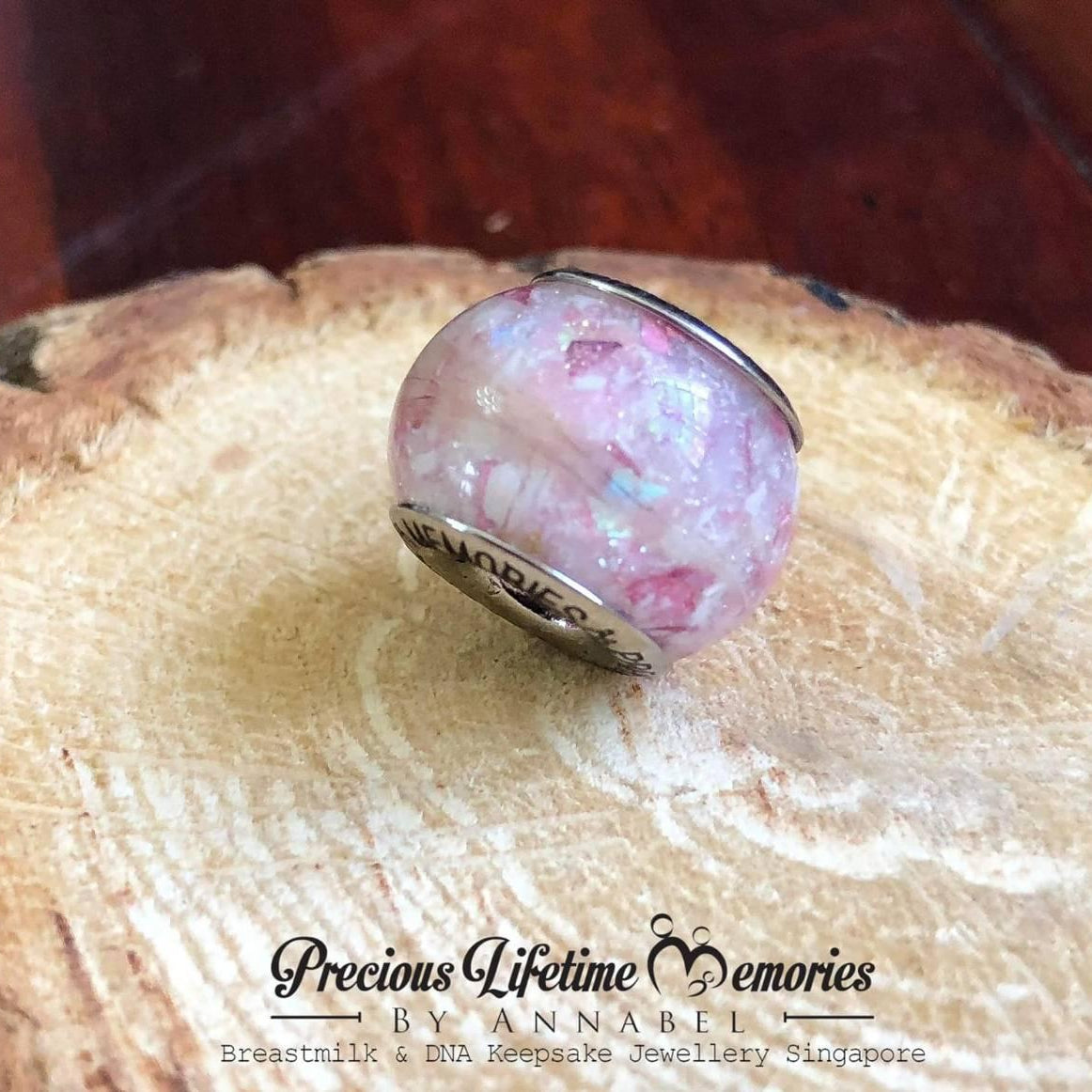 Pink glass charm on a wooden surface with pet and animal ashes and fur charm. 'Precious Lifetime Memories' branding.