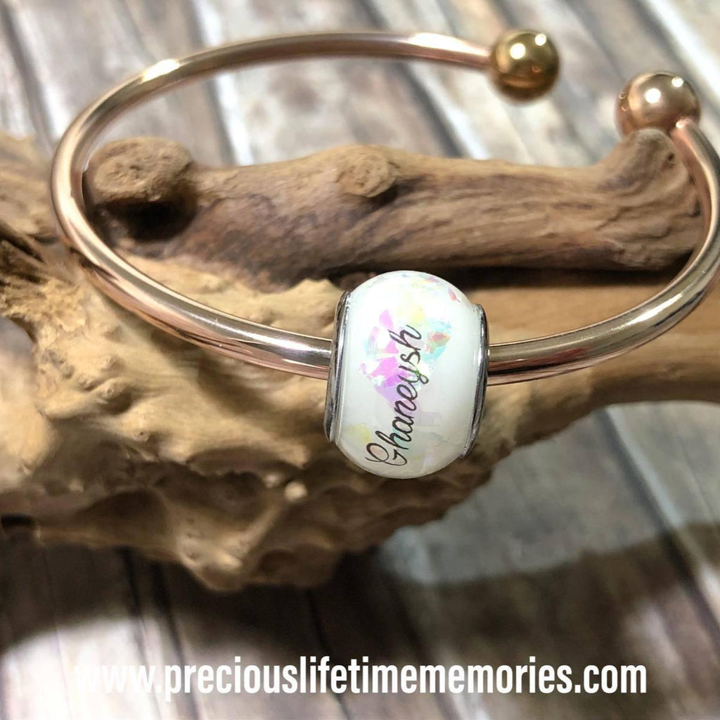 Silver bracelet with a charm featuring 'Chanel' on a wooden surface.