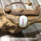 Silver bracelet with a charm featuring 'Chanel' on a wooden surface.