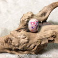 Pink glass bead on a piece of driftwood with a white background