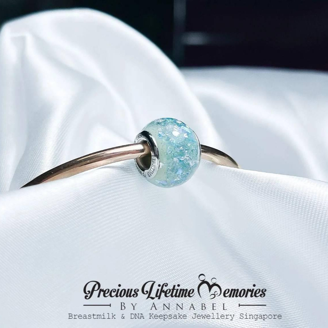 Jewelry with a blue gemstone on a white fabric background, branded 'Precious Lifetime Memories by Annabel'.