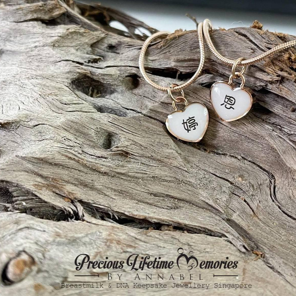 Two heart-shaped pendants on gold necklaces with engraved text, placed on driftwood.