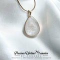 Teardrop-shaped pendant on a gold chain against a white satin background, with 母乳首饰