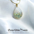 Teardrop-shaped pendant with gold frame on a white fabric background, featuring 'Precious Lifetime Memories by Annabel' branding.