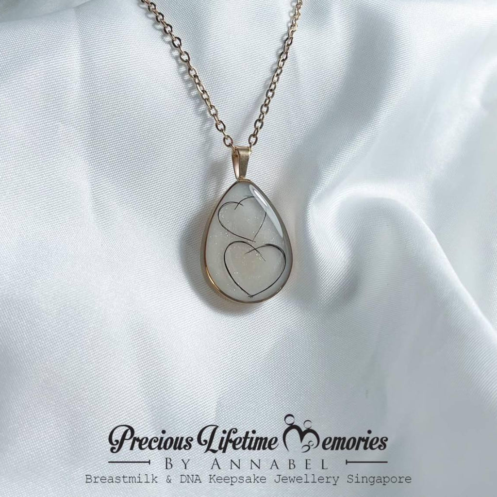 Teardrop-shaped pendant with heart design on a white fabric background, featuring 'Previous Lifetime Memories by Annabel'.