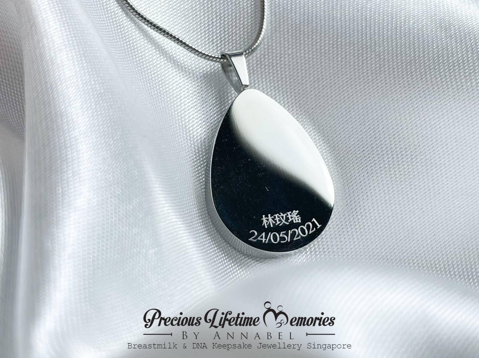 Teardrop-shaped pendant with engraved text on a white fabric background, featuring 'Precious Lifetime Memories by Annabel'.