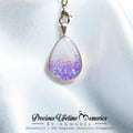 Teardrop-shaped pendant with purple and white gradient on a white fabric background, branded 'Precious Lifetime Memories by Annabel'.