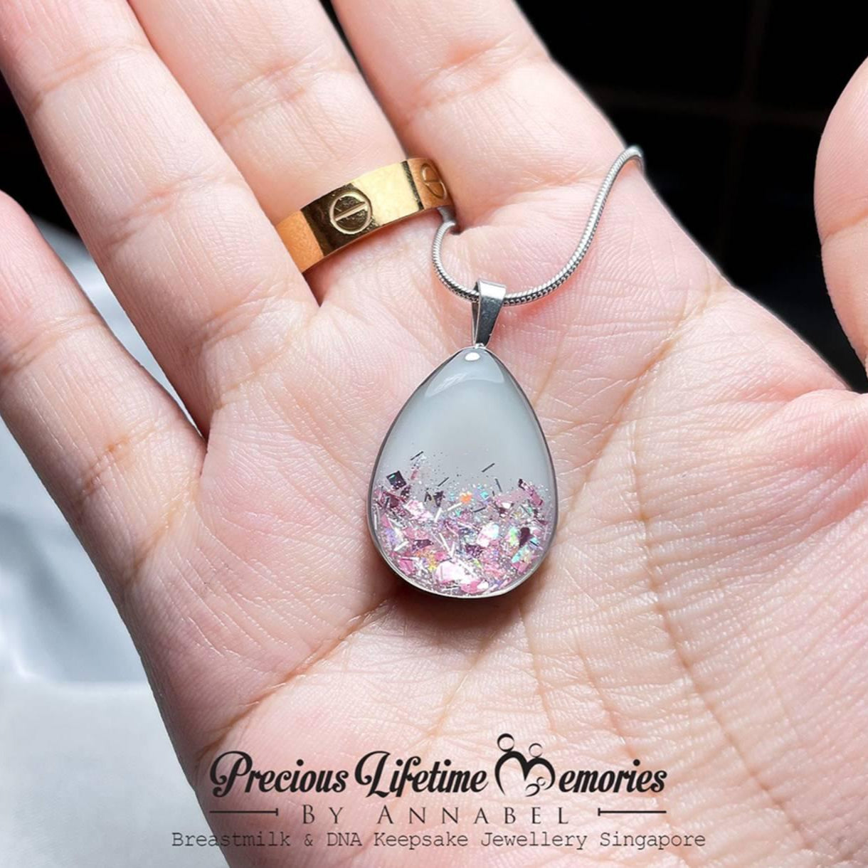 Teardrop-shaped pendant with glittery design held in a hand, branded 'Precious Lifetime Memories by Annabel'.