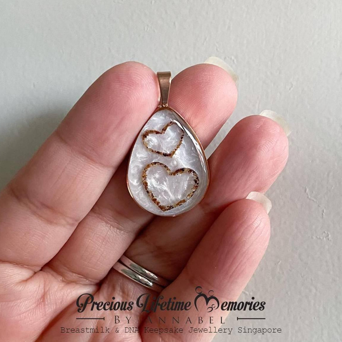 Hand holding a silver pendant with heart designs against a plain background breastmilk droplet 母乳水滴