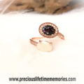 Rose gold ring with a dark gemstone on a white surface, brand 'precious lifetime memories' visible.