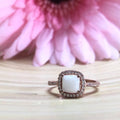 Rose gold ring with a large gemstone in front of a pink flower on a wooden surface.
