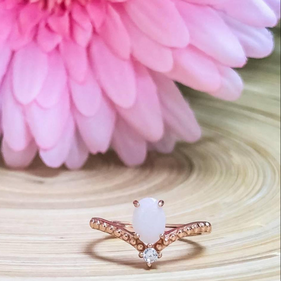 Rose gold ring with pink gemstone on a wooden surface with a pink flower in the background