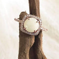 Silver and rose gold ring with a breastsmith stone on a wooden branch against a soft background.