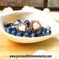 Heart-shaped earrings with blue beads in a shell on a wooden surface, brand 'preciouslifetimememories' visible.