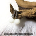 Pair of earrings with white spherical beads on a wooden surface
