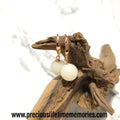 Rose gold earrings with white beads on a piece of driftwood against a white background.