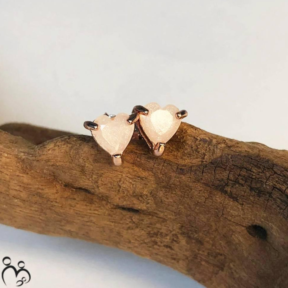 Heart-shaped breast milk earrings on a piece of wood with a light background