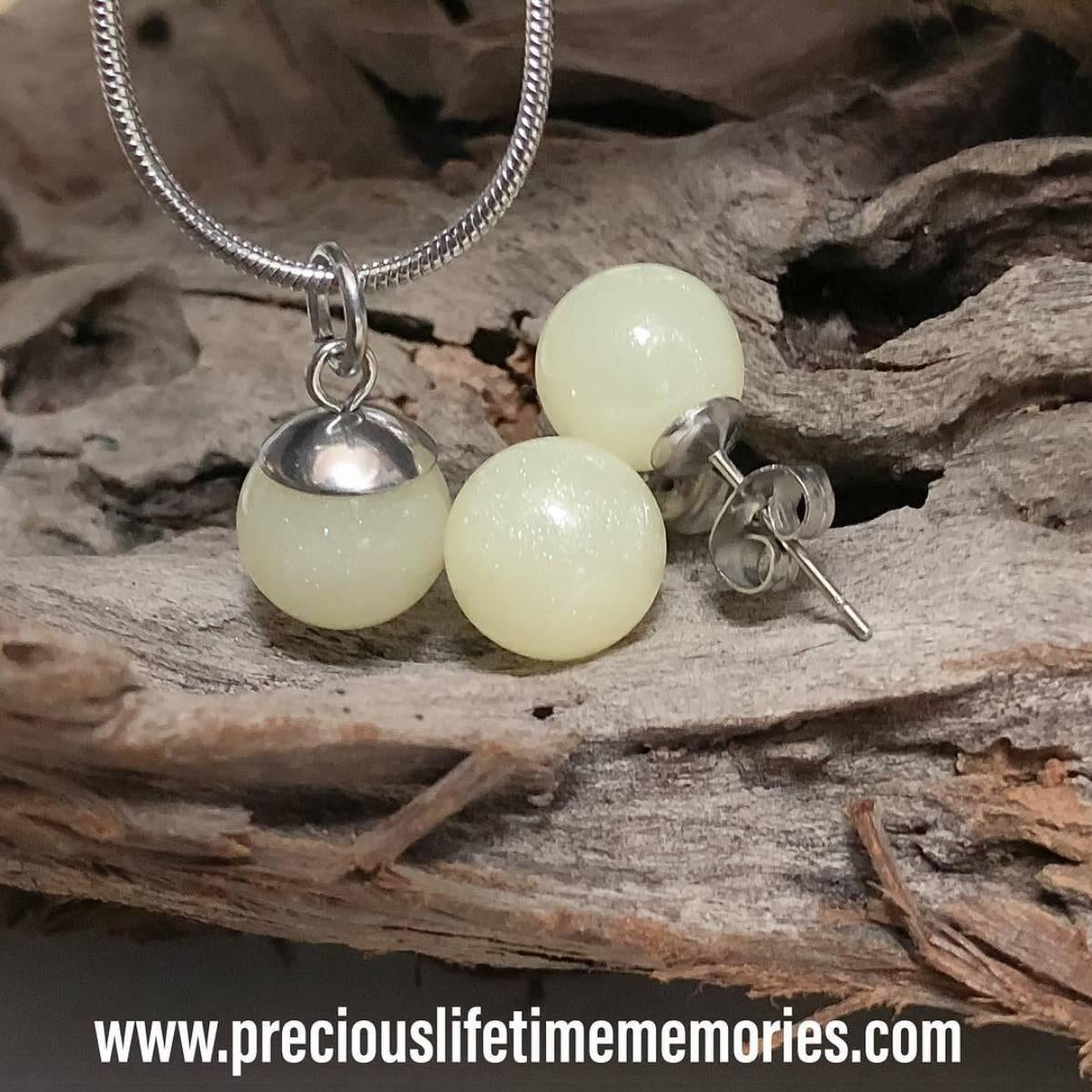 Pair of light green spherical earrings with silver accents on a wooden surface.
