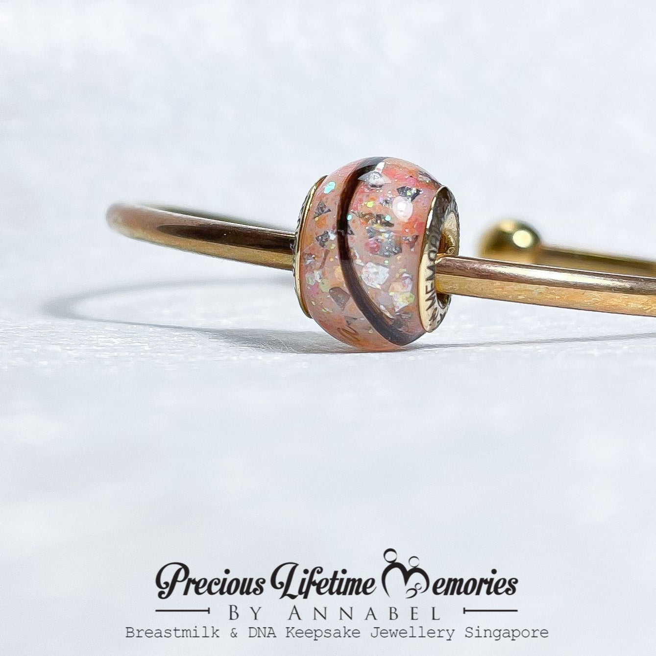 Gold bracelet with a pink charm on a white background, featuring 'Precious Lifetime Memories by Annabel' branding.