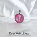 Pink pendant with letter 'J' on a white satin background, branded 'Precious Lifetime Memories by Annabel'.