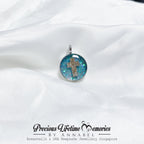 Pendant with a cross design on a white fabric background, featuring 'Precious Lifetime Memories by Annabel'.