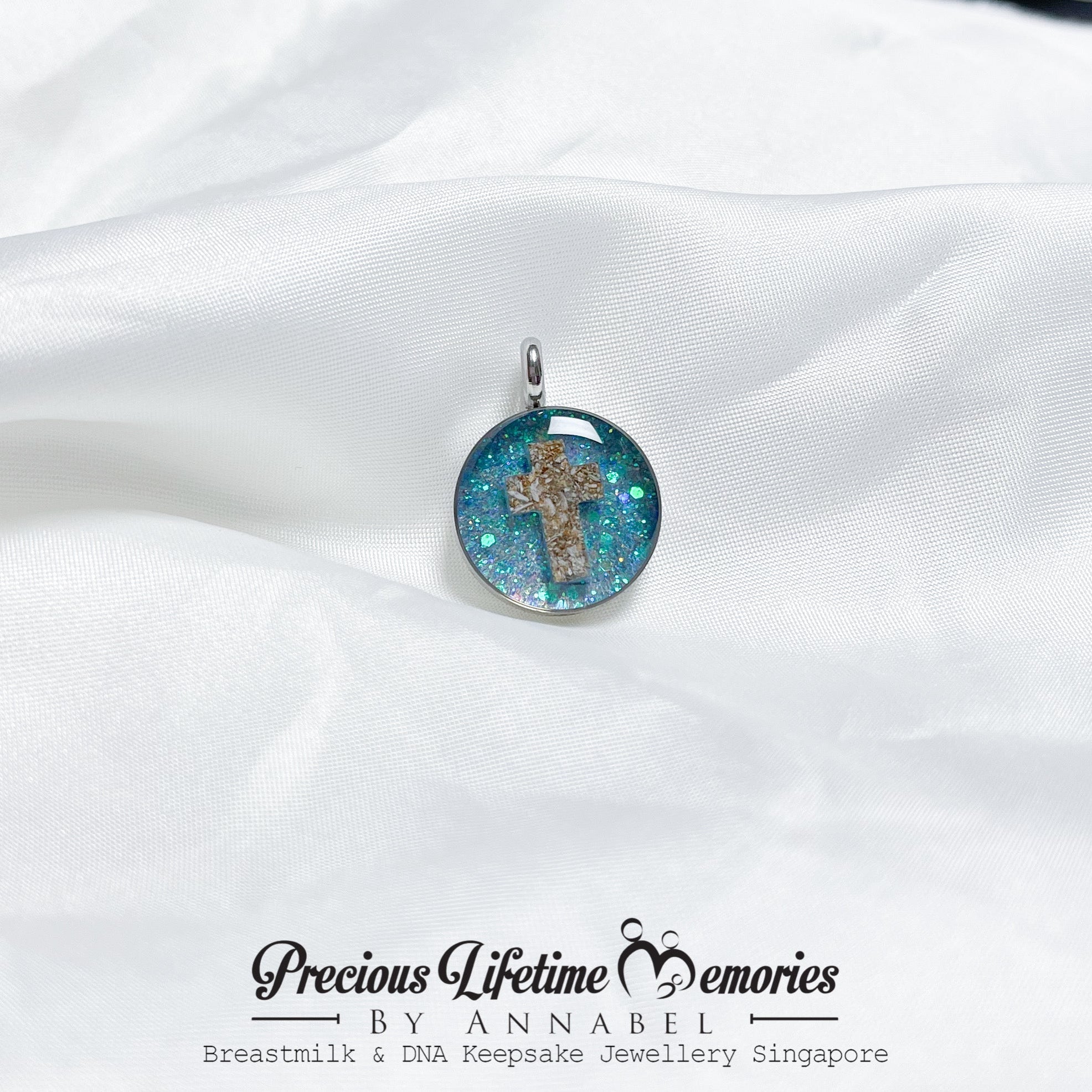 Pendant with a cross design on a white fabric background, featuring 'Precious Lifetime Memories by Annabel'.