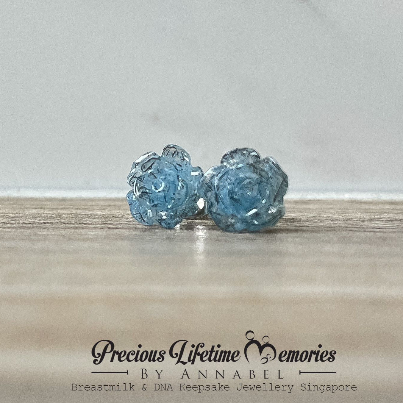 Pair of blue crystal stud earrings on a wooden surface with 'Precious Lifetime Memories by Annabel' branding.