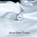 Silver pendant with floral design and 'Bibi' engraving on white fabric, branded 'Precious Lifetime Memories by Annabel'.