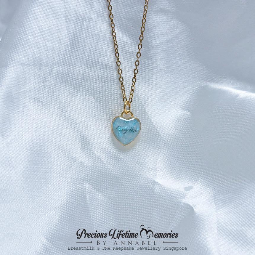 Heart-shaped necklace with blue pendant on a white fabric background, branded 'Precious Lifetime Memories by Annabel'.